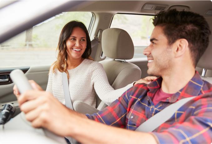 A man in a driver's seat with a woman in the passenger seat smiling at each other