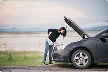 A woman on the side of the road with an open hood of a car