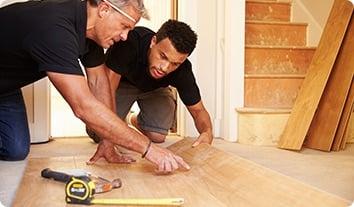 a couple of men working on a wood floor