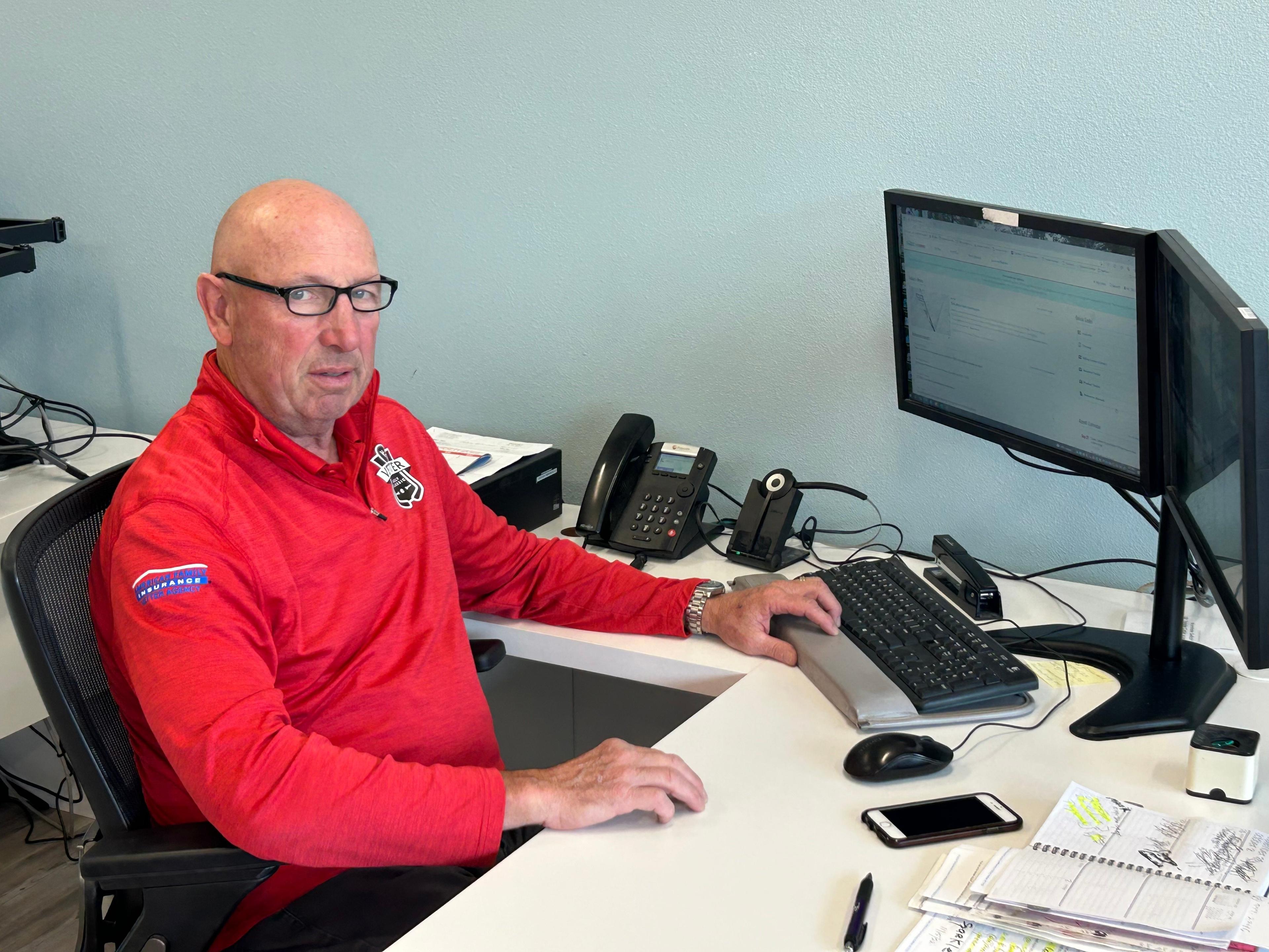 John Hagenstein sitting at a desk with a computer and a phone