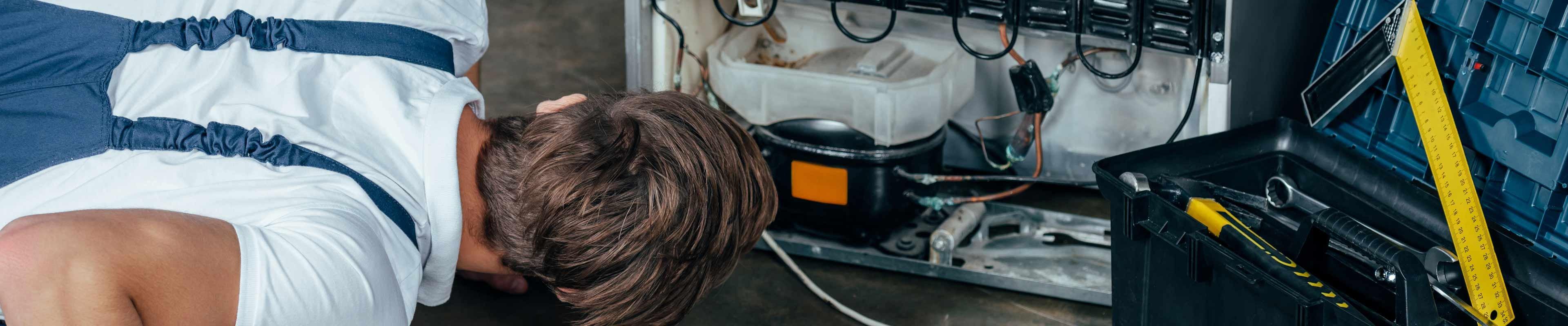 Man on floor looking at base of a refrigerator