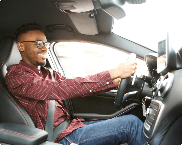 A smiling rideshare driver, driving their vehicle on a sunny day.  