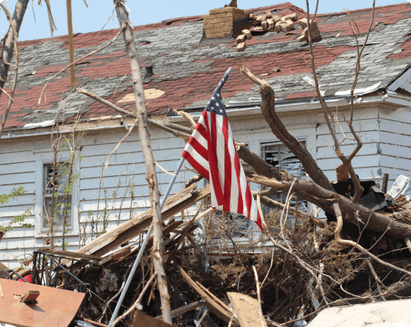 An American flag, standing in home-wreckage after a storm.