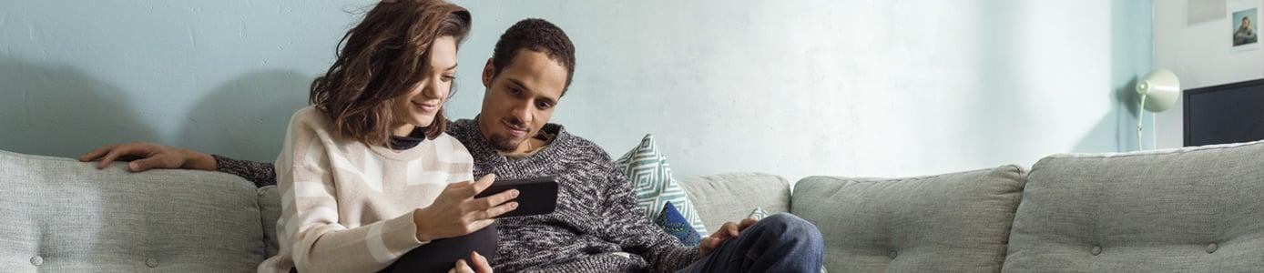 Couple sitting on couch setting up their smart home on their phone