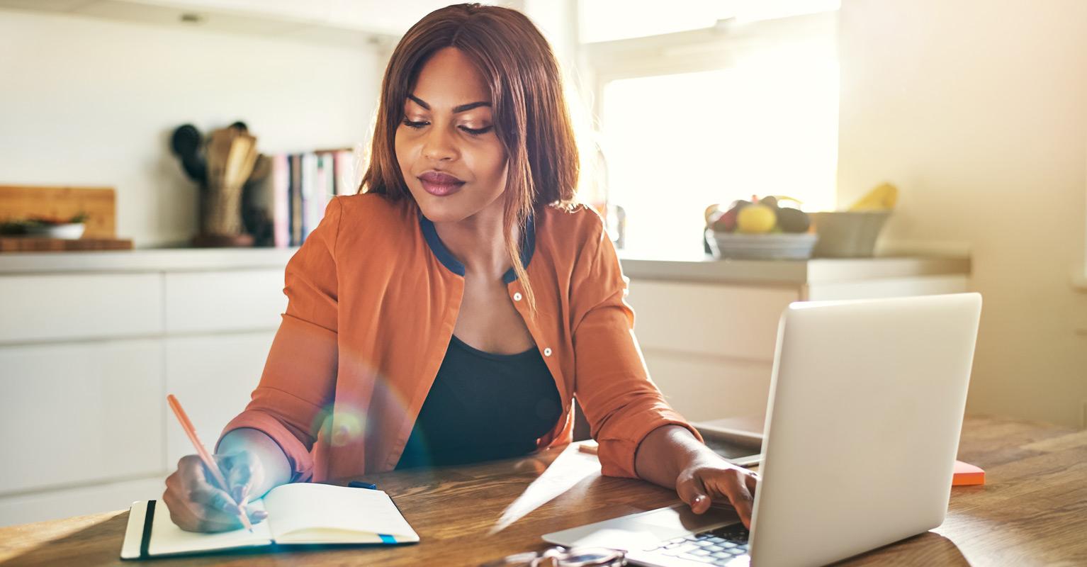 Woman sitting at table writing a home inventory for homeowners insurance. 