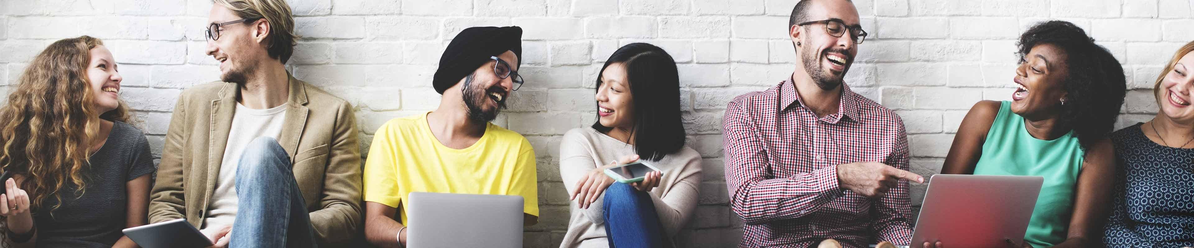 An ethnically diverse group of happy people sitting on the floor networking for business.