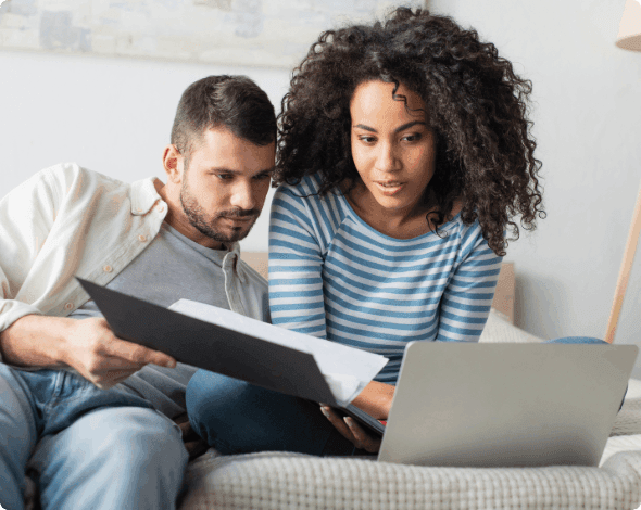 A couple reviewing documents while sitting in front of a laptop.